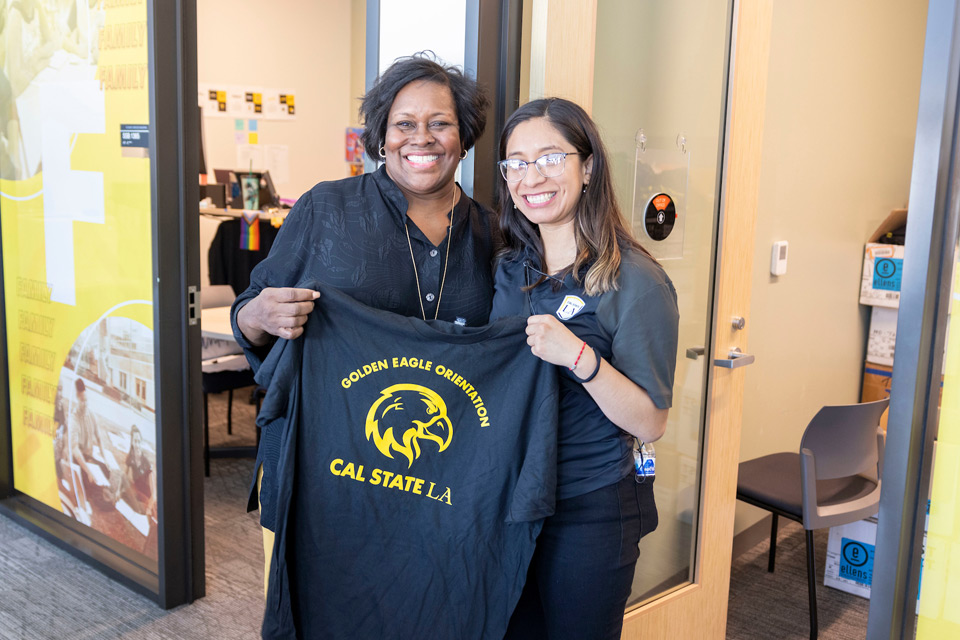 President Eanes takes a photo with a Cal State LA staff member while holding up a "Golden Eagles Orientation" t-shirt.